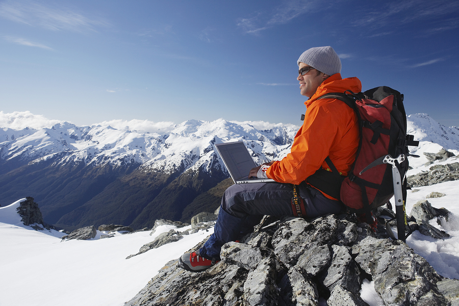 Side view of a male mountain climber using laptop on mountain pe